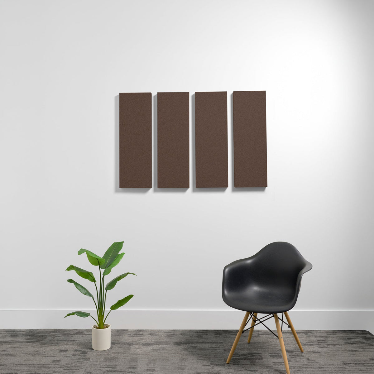 Four brown rectangular 3D acoustic panels mounted on white wall above black chair and potted plant.