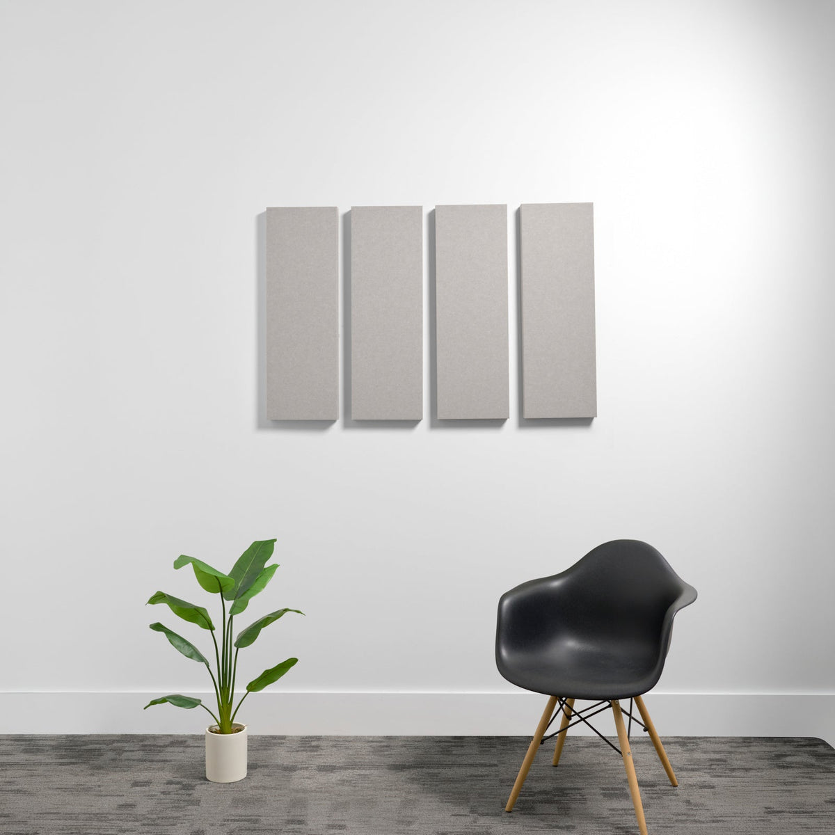 Four rectangular gray acoustic panels mounted on a white wall above a black chair and potted plant.