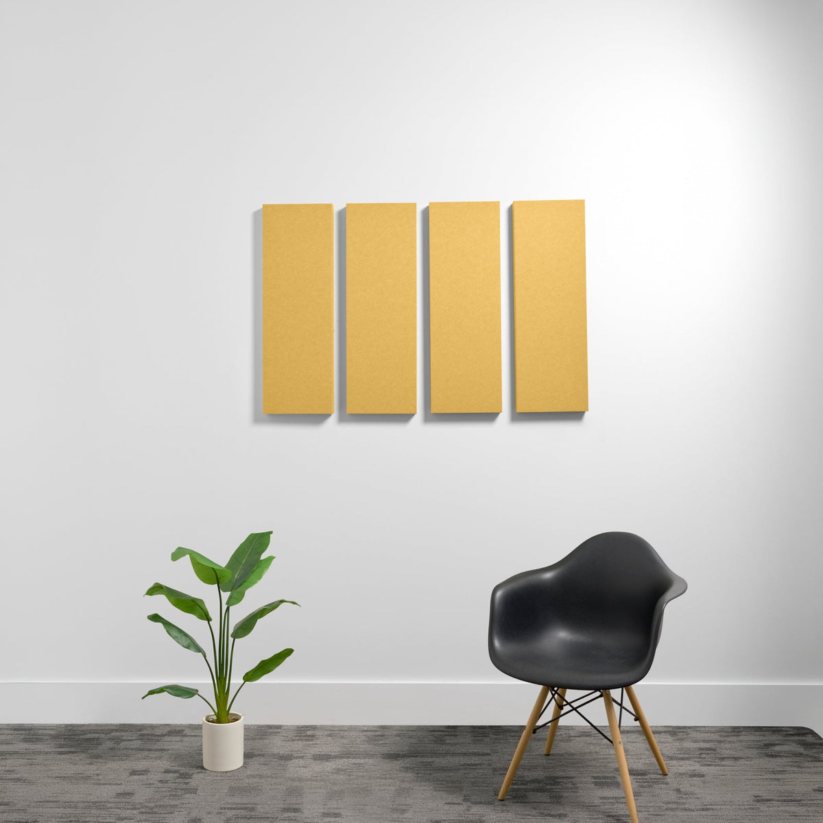 Four rectangular yellow acoustic panels mounted on white wall above black chair and potted plant.