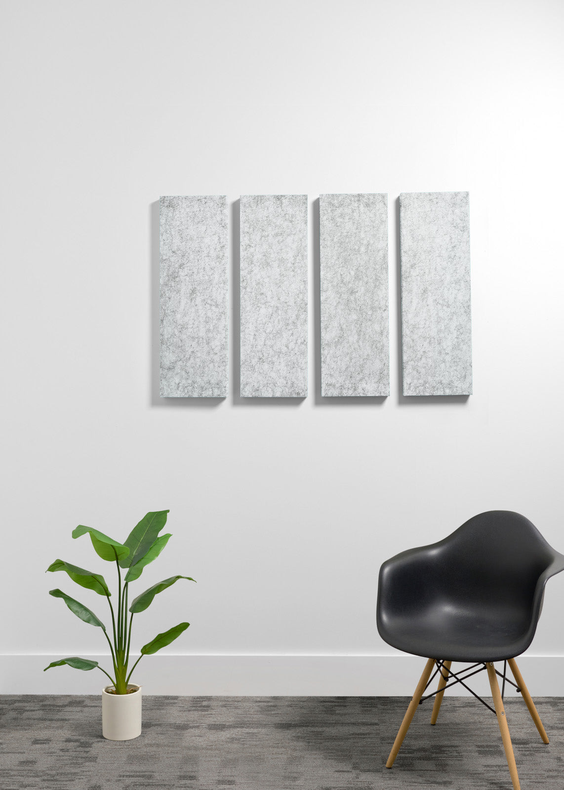 A four-panel vertical canvas wall art set with a textured light gray and white pattern, displayed on a white wall in a modern room setting with a black chair and a potted plant.