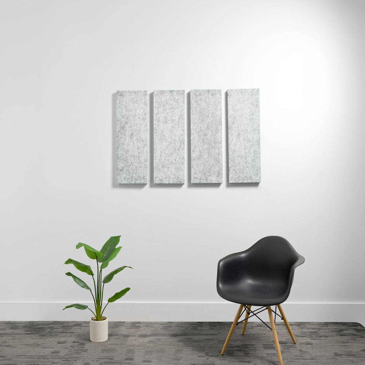 Four gray rectangular acoustic panels mounted vertically on a white wall above a black chair and potted plant.