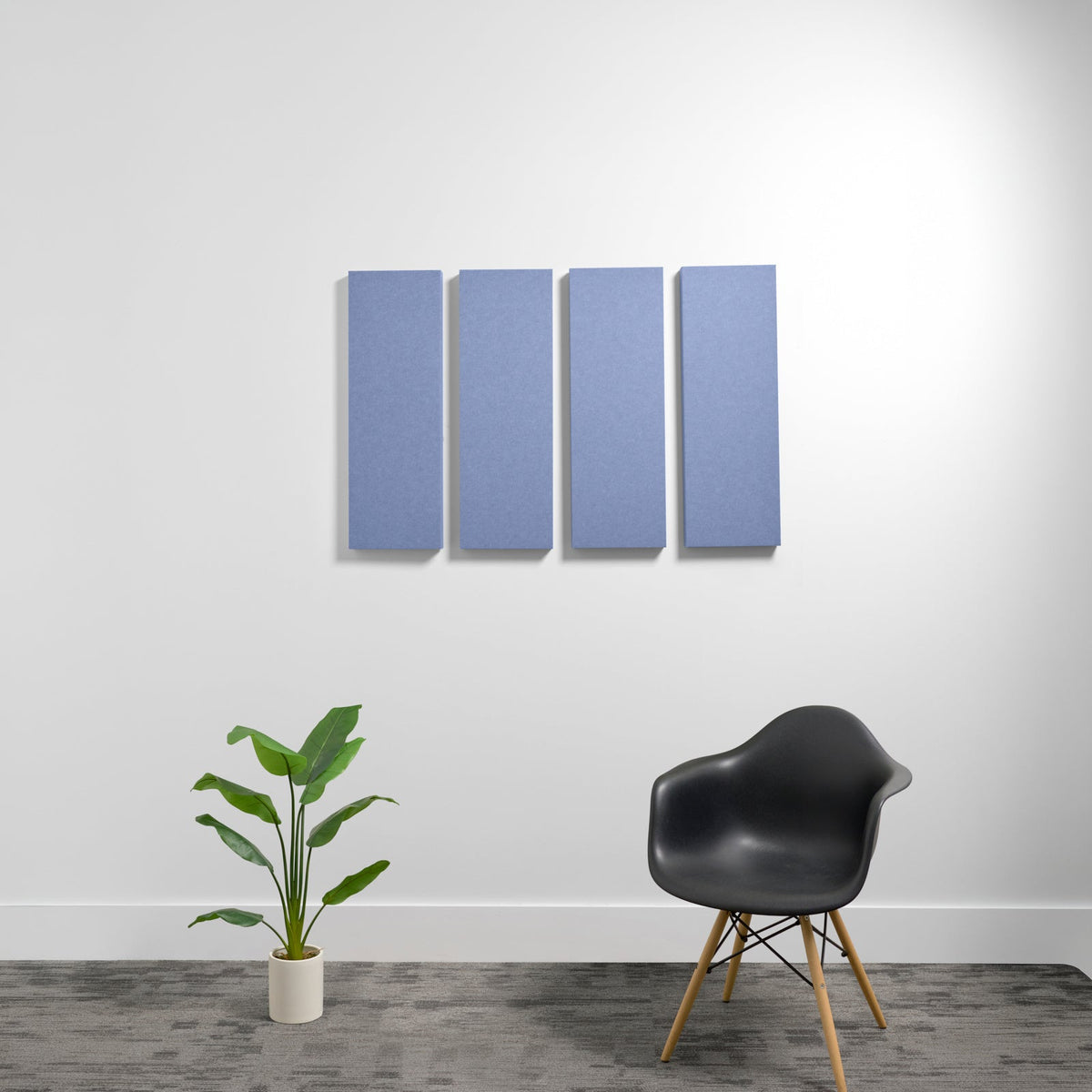 Four blue rectangular acoustic panels mounted on white wall above black chair and potted plant.
