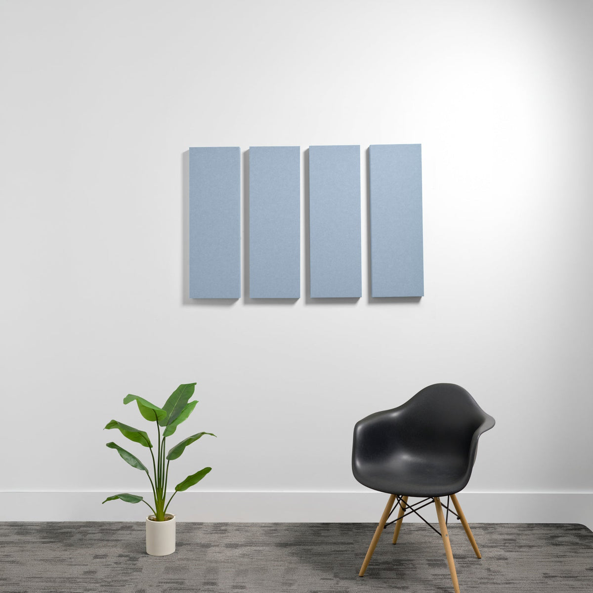 Four blue-gray rectangular acoustic panels mounted on white wall above black chair and potted plant.
