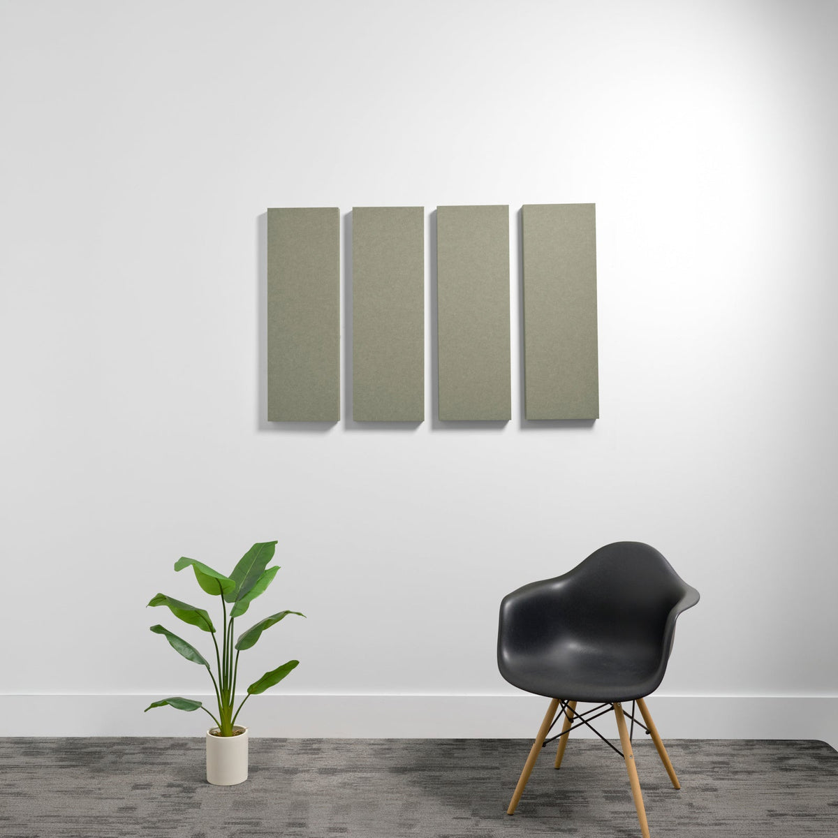Four rectangular sage green acoustic wall panels mounted on white wall above black chair and potted plant.