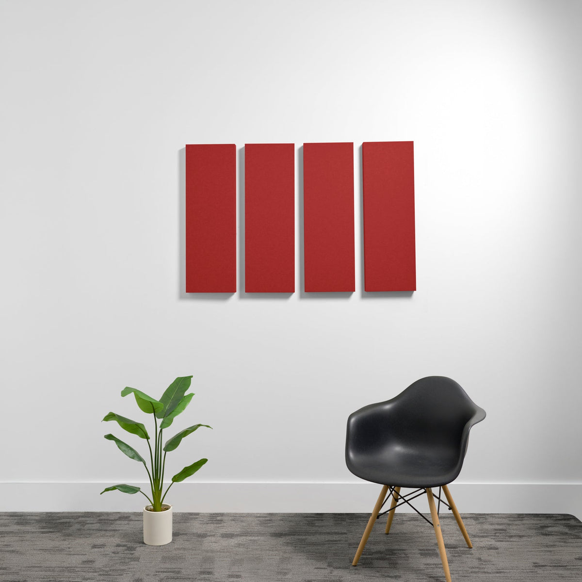 Four red rectangular 3D acoustic panels mounted on a white wall above a black chair and potted plant.