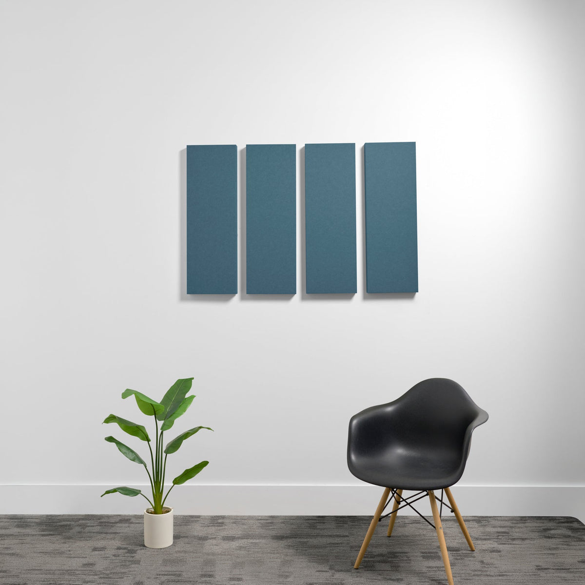 Four rectangular teal acoustic panels mounted on white wall above black chair and potted plant.