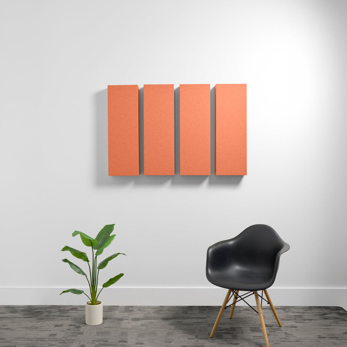 Four rectangular orange acoustic panels mounted on wall above black chair and potted plant.