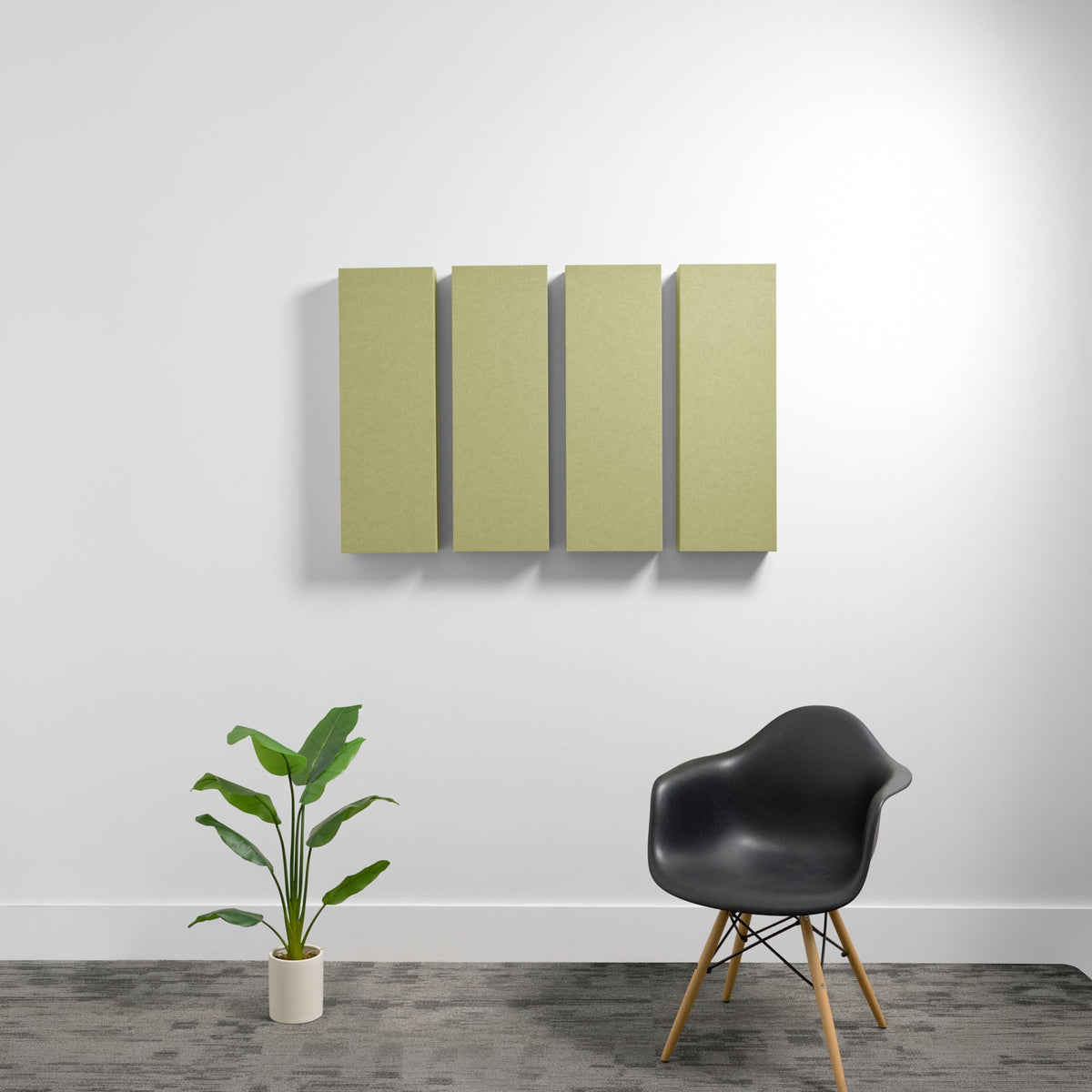 Four vertical rectangular acoustic panels in sage green mounted on white wall above black chair and potted plant.