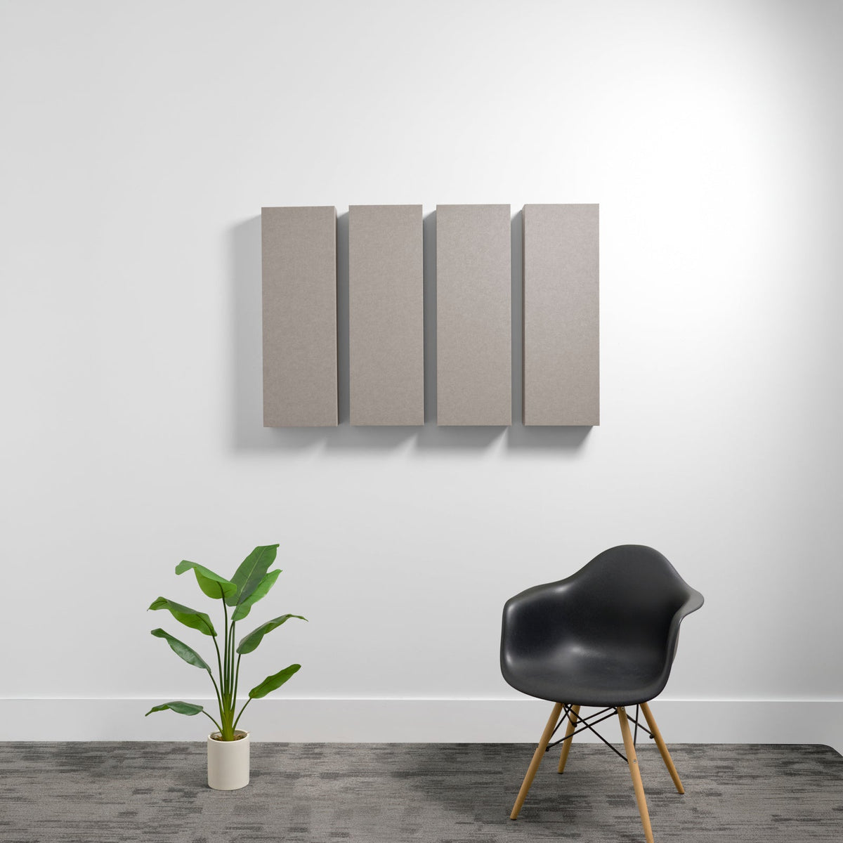 Four rectangular gray acoustic panels mounted on wall above black chair and potted plant.