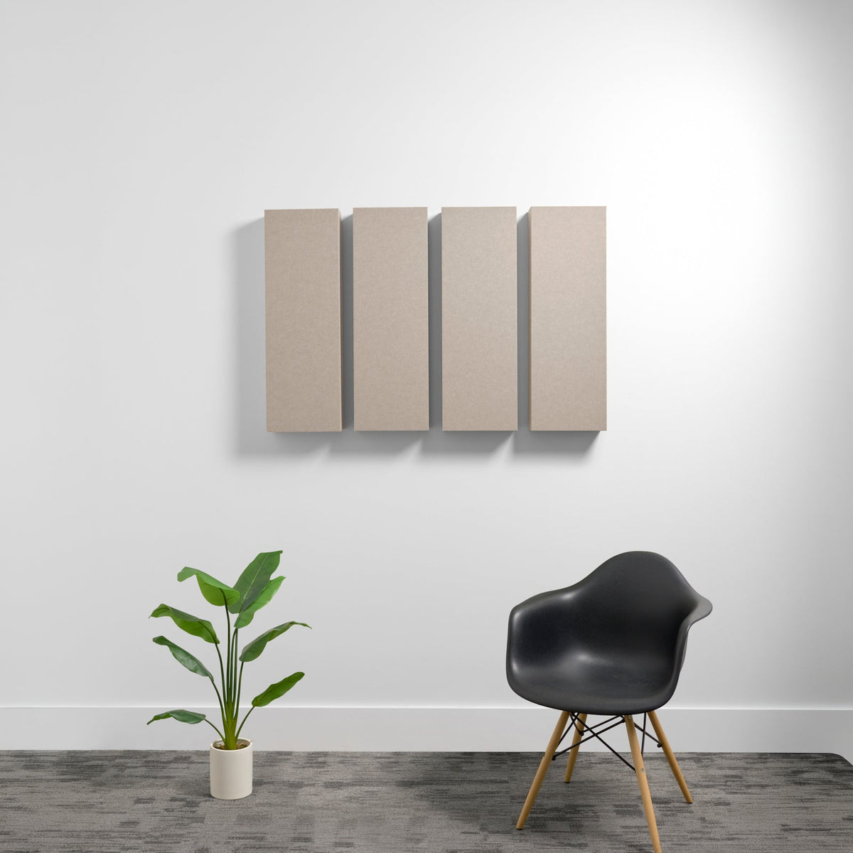 Four beige rectangular acoustic panels mounted on white wall above black chair and potted plant.