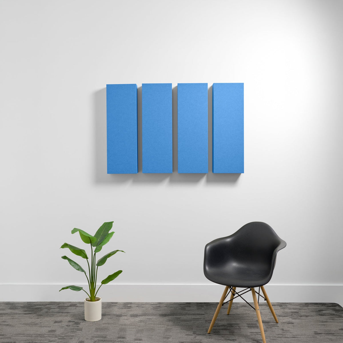 Four blue rectangular acoustic panels mounted on a white wall above a black chair and potted plant.