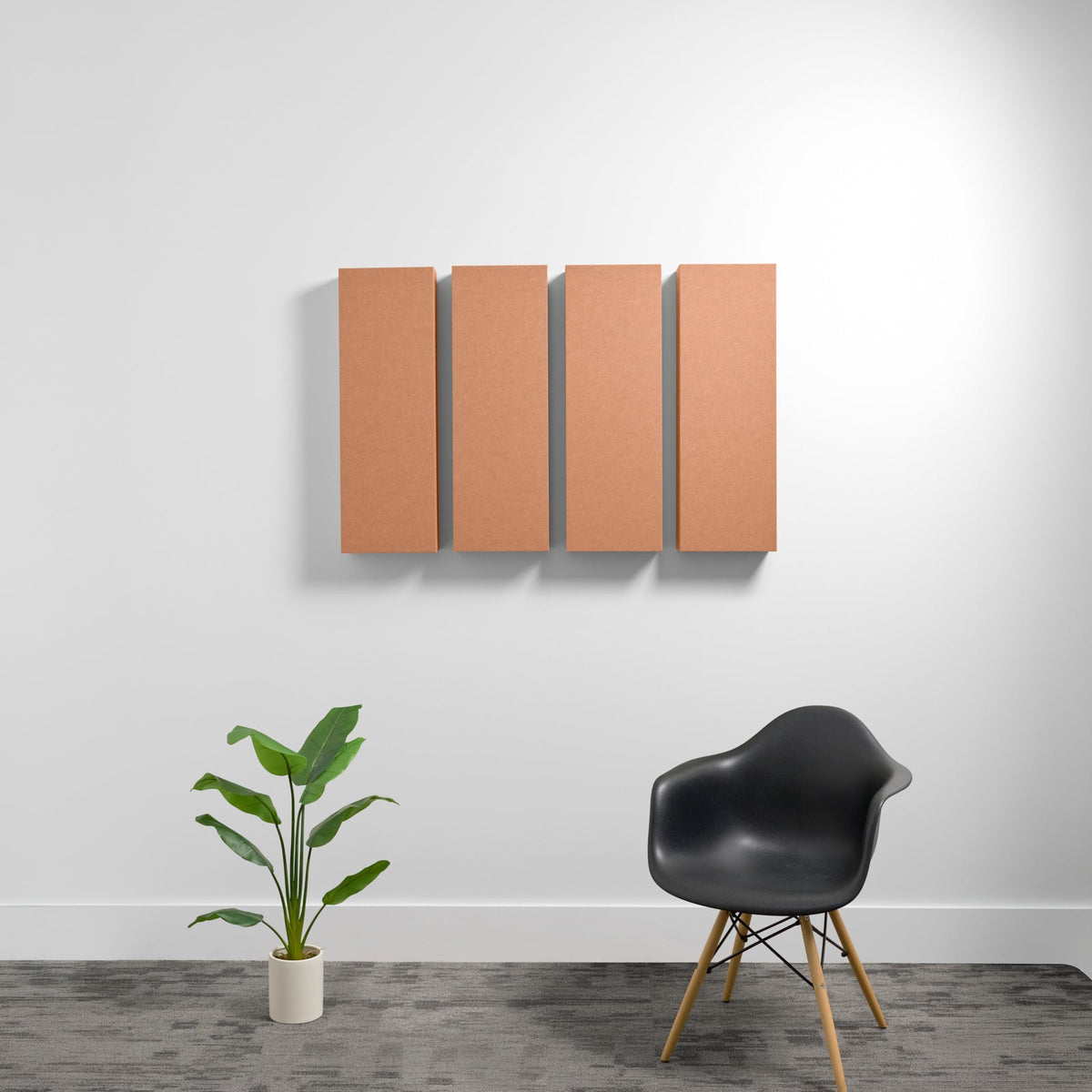 Four rectangular tan acoustic panels mounted on white wall above black chair and potted plant.