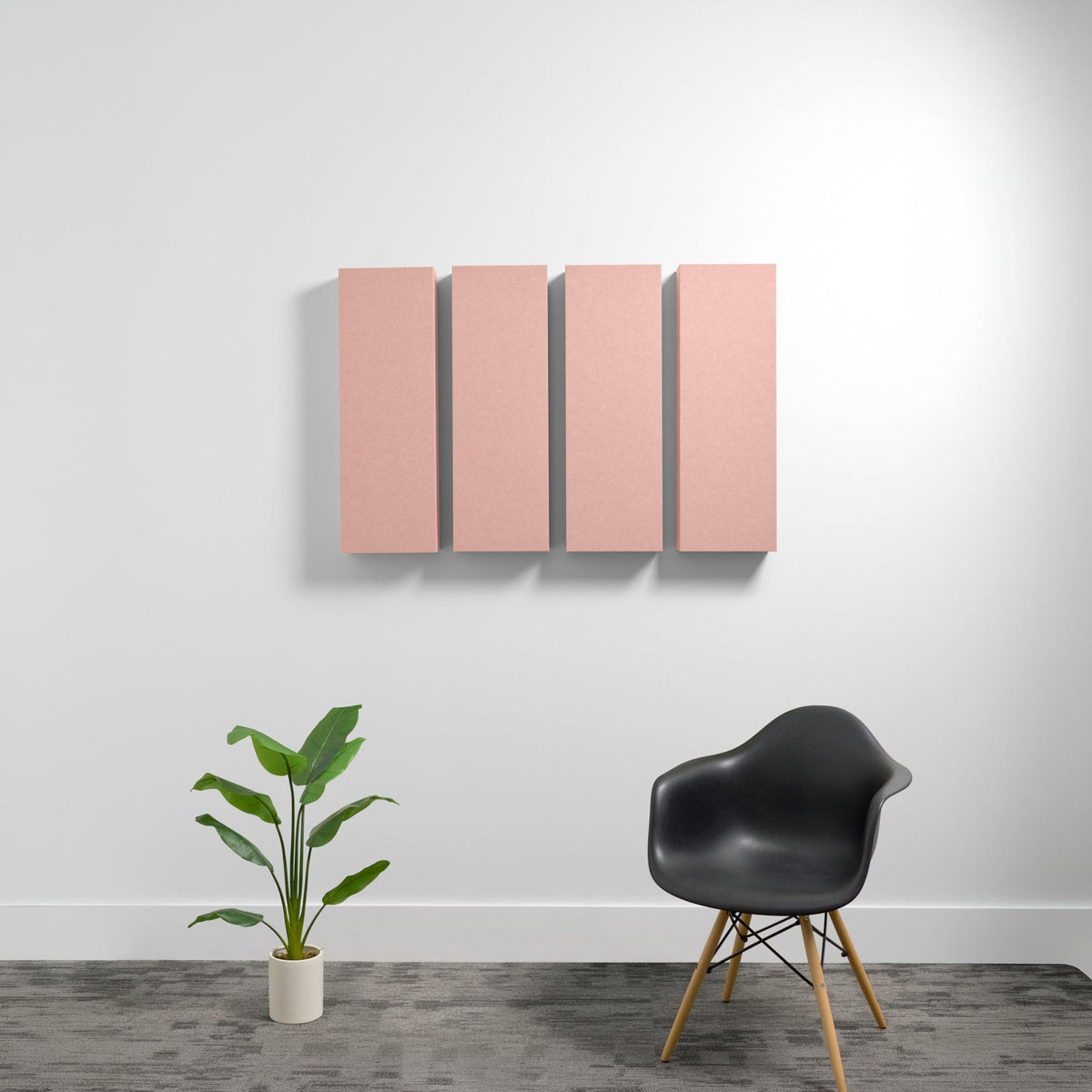 Four pink rectangular acoustic panels mounted on white wall above black chair and potted plant.
