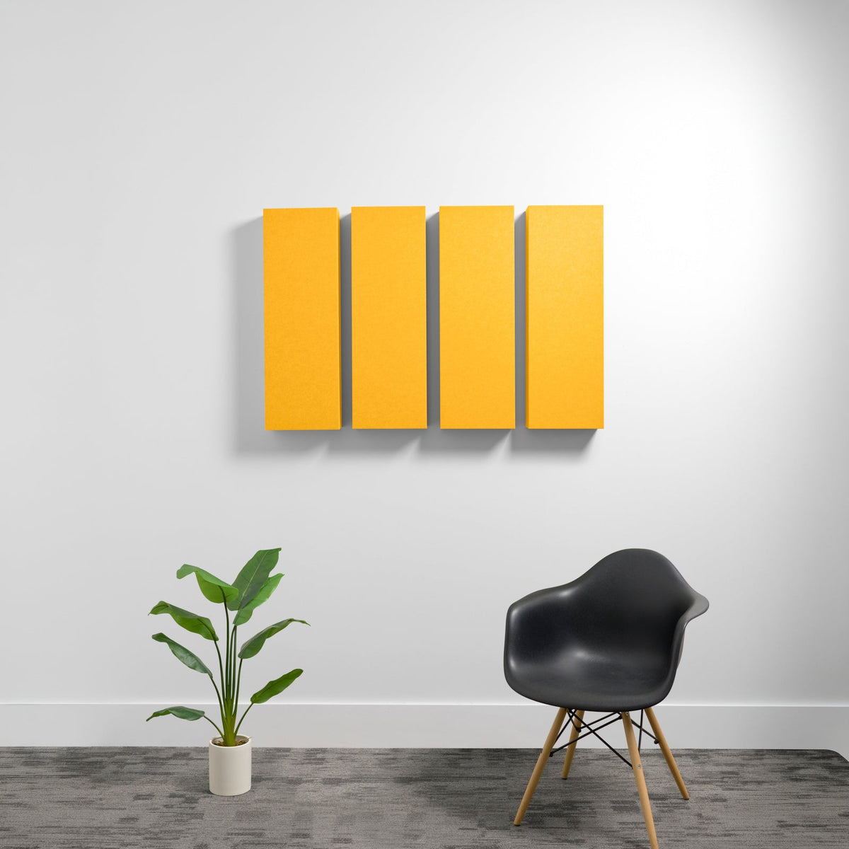 Four yellow rectangular acoustic panels mounted on a white wall above a black chair and potted plant.