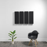 Four black rectangular 3D acoustic panels mounted on white wall above a chair and plant.