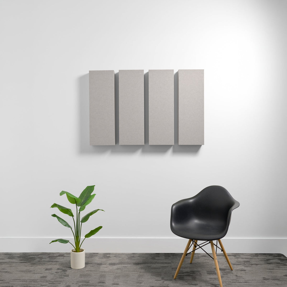 Four rectangular beige acoustic panels mounted on wall above black chair and potted plant.