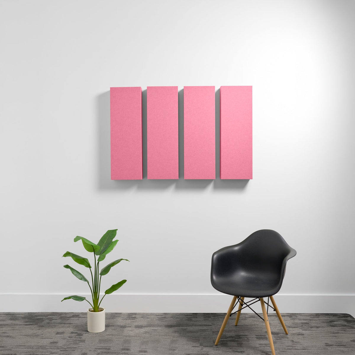 Four pink rectangular acoustic panels mounted on white wall above black chair and potted plant.