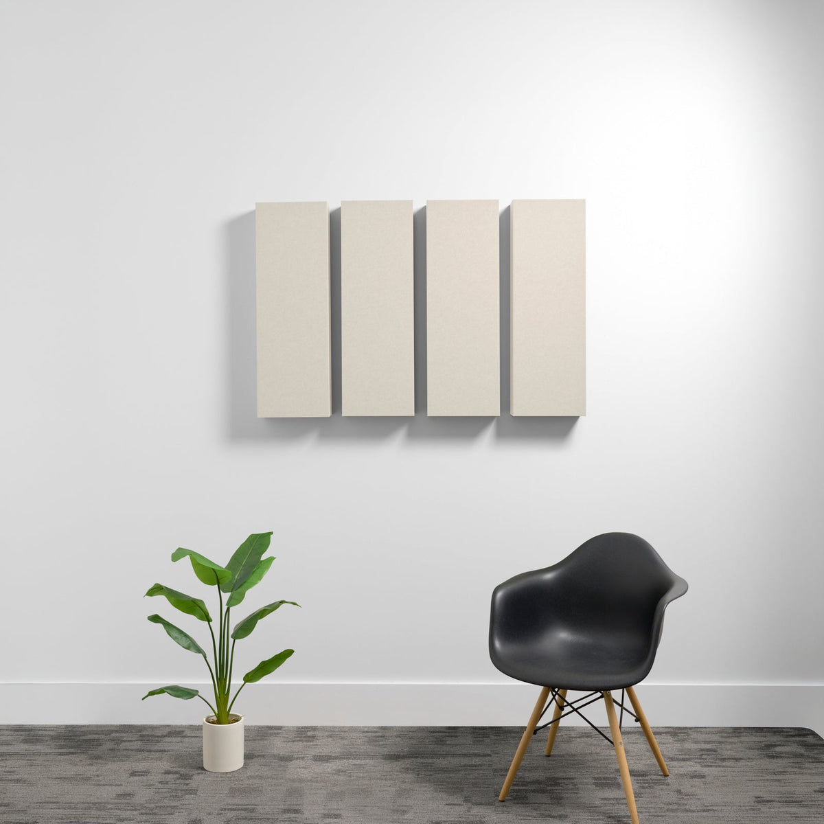 Four cream-colored rectangular acoustic panels mounted on wall above black chair and potted plant.