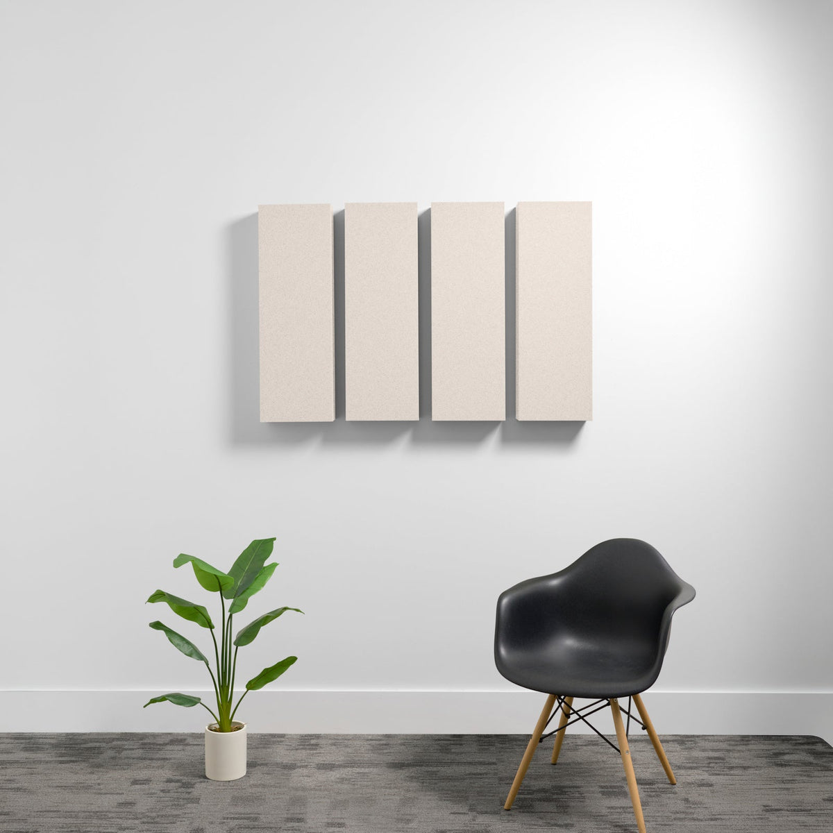 Four beige rectangular acoustic panels mounted on wall above black chair and potted plant.