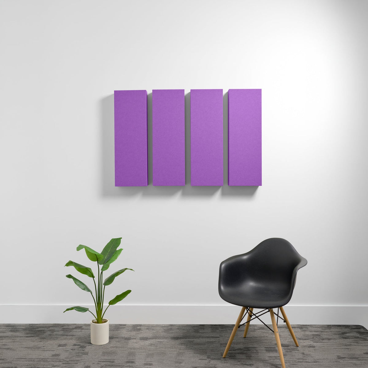 Four purple rectangular acoustic panels mounted on white wall above potted plant and black chair.