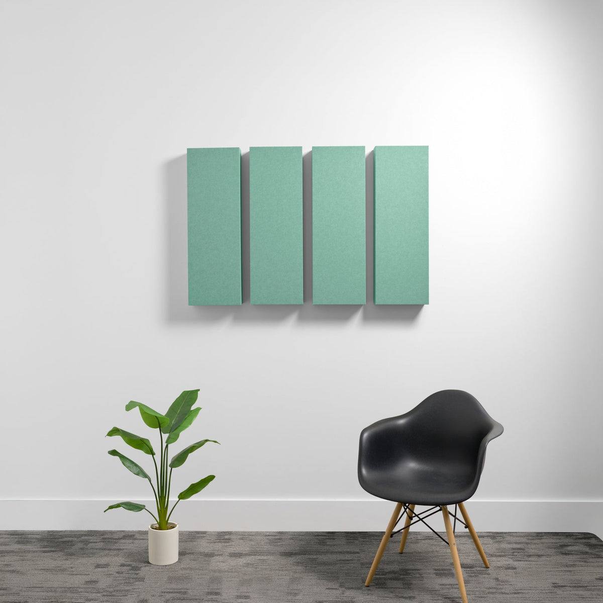 Four rectangular sage green acoustic panels mounted on white wall above black chair and potted plant.