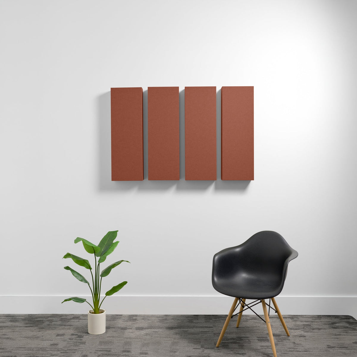 Four rectangular terracotta acoustic panels mounted on wall above black chair and potted plant.