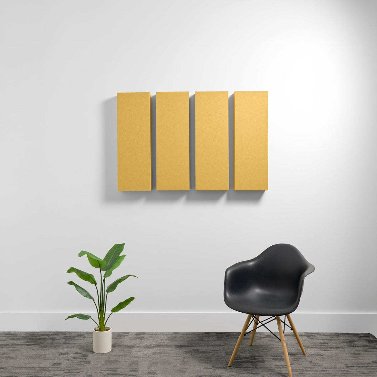 Four rectangular golden-yellow acoustic panels mounted on a white wall above a black chair and potted plant.