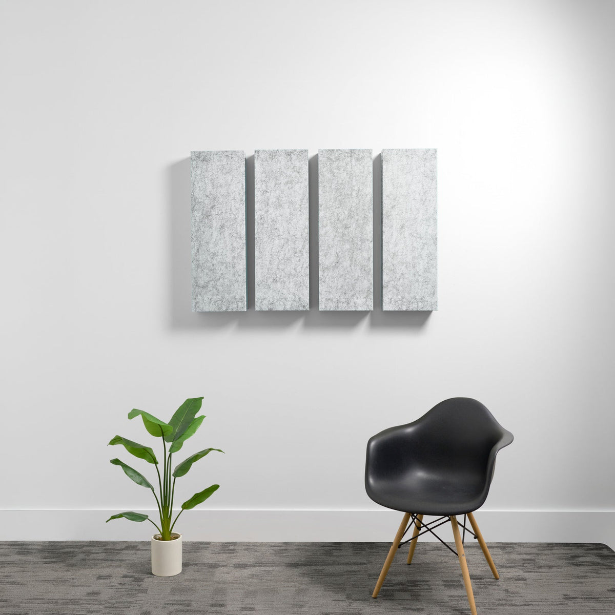 Four gray rectangular acoustic panels mounted on wall above black chair and potted plant.