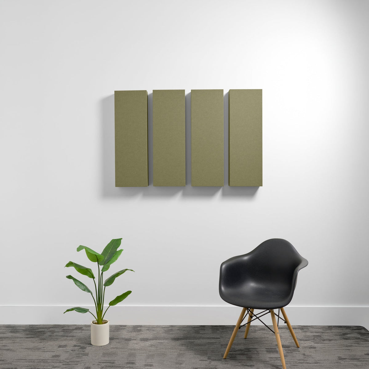 Four rectangular olive-green acoustic panels mounted on white wall above black chair and potted plant.