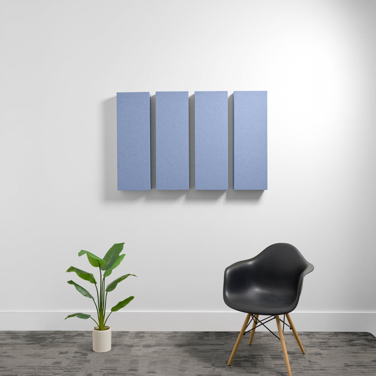 Four blue rectangular acoustic panels mounted on white wall above black chair and potted plant.