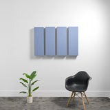 Four blue rectangular acoustic panels mounted on white wall above black chair and potted plant.