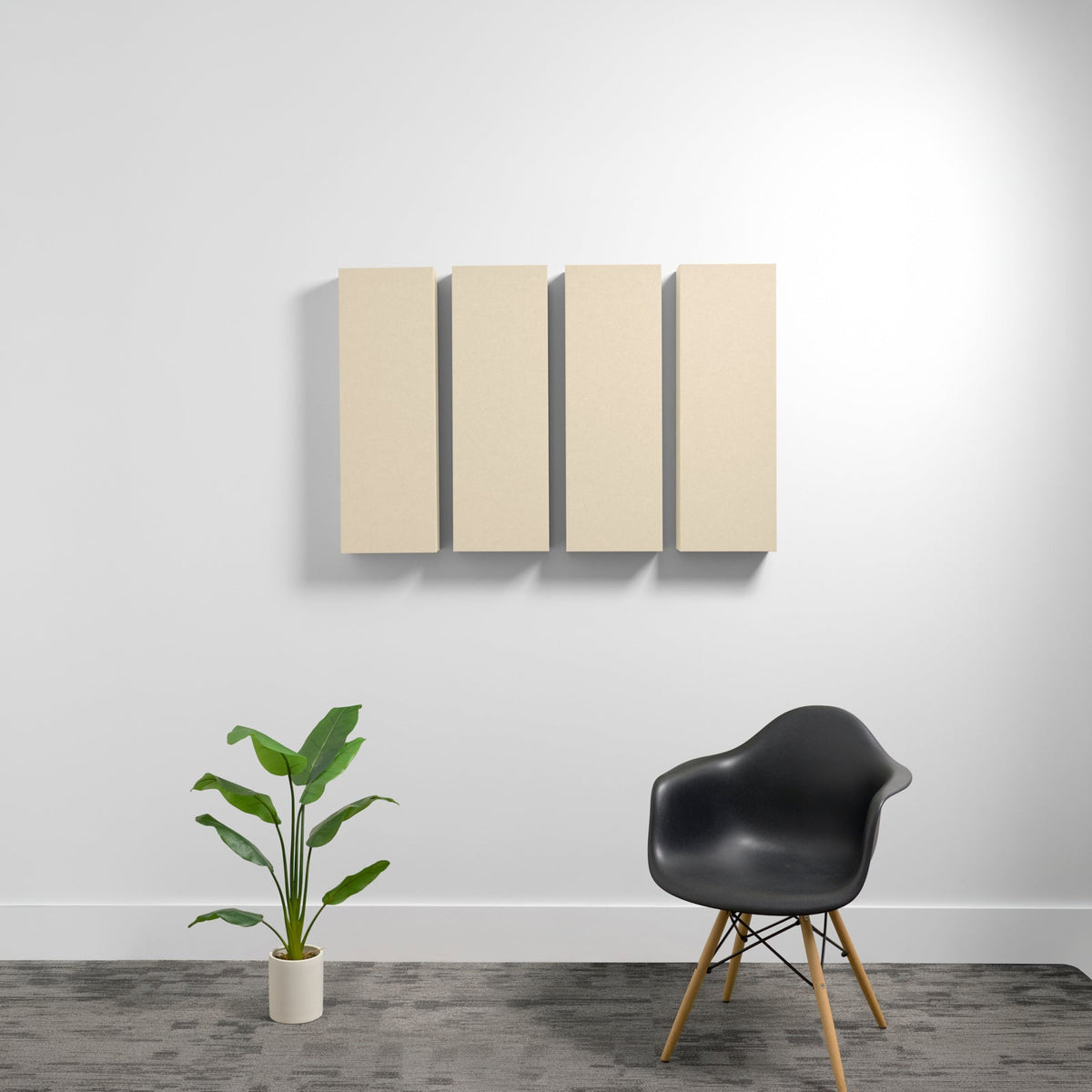 Four beige rectangular acoustic panels mounted on a white wall above a black chair and potted plant.