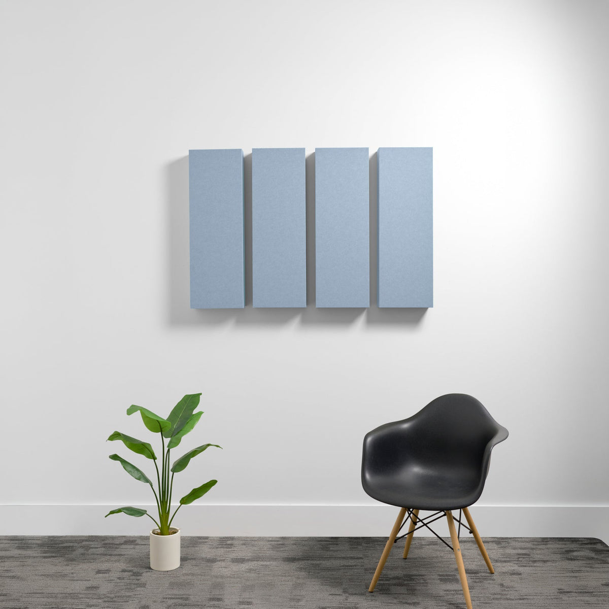 Four blue-gray rectangular acoustic panels mounted on wall above potted plant and black chair.