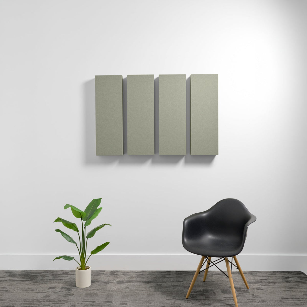 Four rectangular sage green acoustic panels mounted on white wall above black chair and potted plant.
