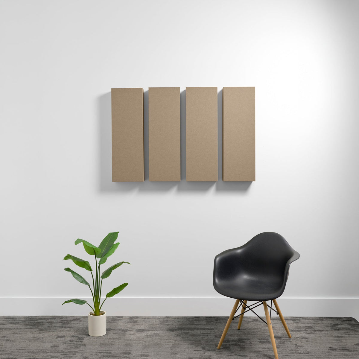 Four tan rectangular acoustic panels mounted on white wall above black chair and potted plant.
