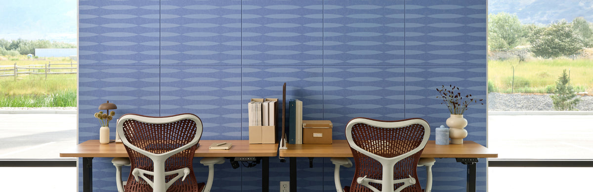 Blue patterned printed acoustic felt panels hung on a wall between windows in a modern open office setting