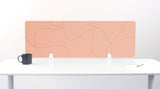 Peach-colored desk divider with abstract topographic line pattern mounted on white desk with black mug and notepad.