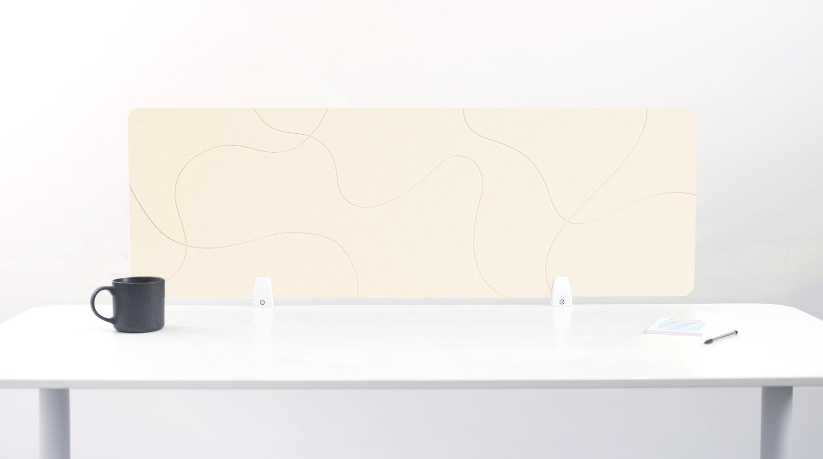 An ivory-colored felt desk divider placed on a white desk with a black mug and a pen beside it.