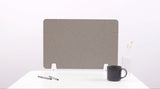 Gray desk divider with curved line pattern, white supports, positioned on white desk with mug and pens.