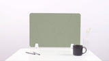 Sage green desk divider with curved line pattern, shown upright on white desk surface with small support feet.