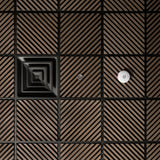 A close-up of a modern wall or ceiling panel featuring a grid pattern of square tiles with diagonal slats in a warm brown tone, separated by black grout lines. One tile has a concentric square design, and another has a small circular metallic fixture.