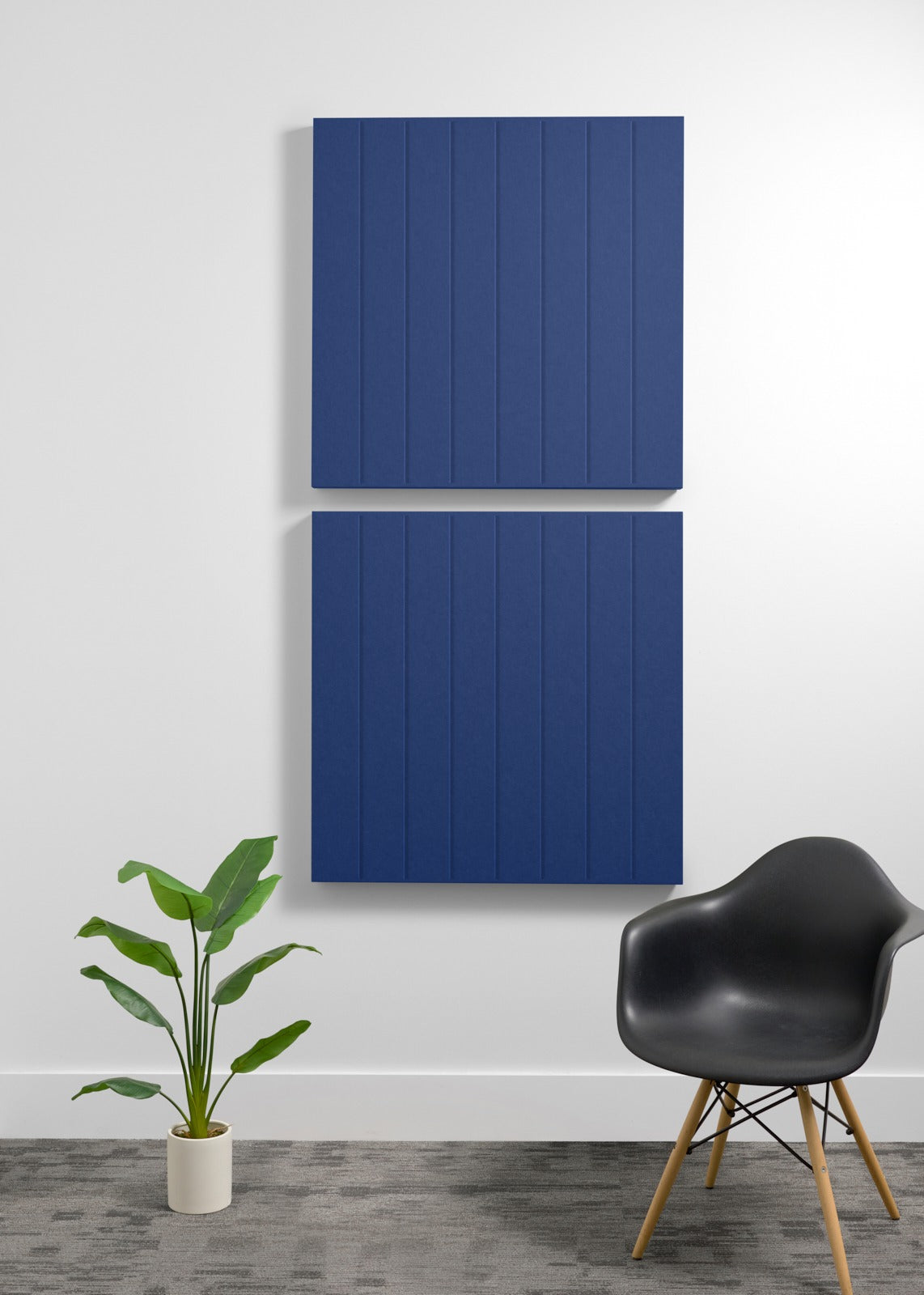 Two stacked navy blue acoustic panels with vertical ribbed texture mounted on wall above chair and plant.