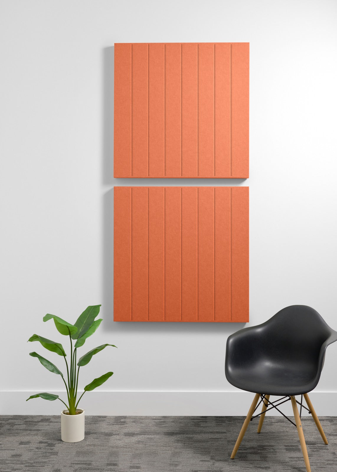 Two stacked terracotta acoustic panels with vertical grooves mounted on a wall above a black chair and potted plant.