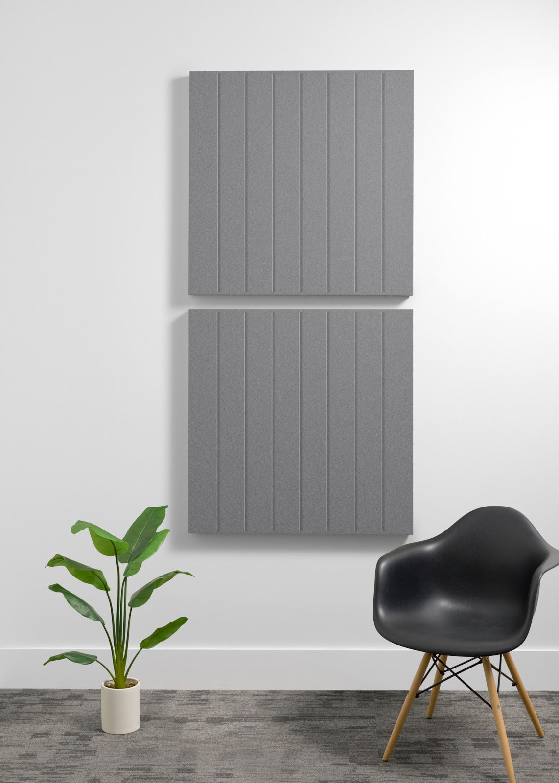 Two stacked gray acoustic panels with vertical ribbed texture mounted on white wall above potted plant and black chair.