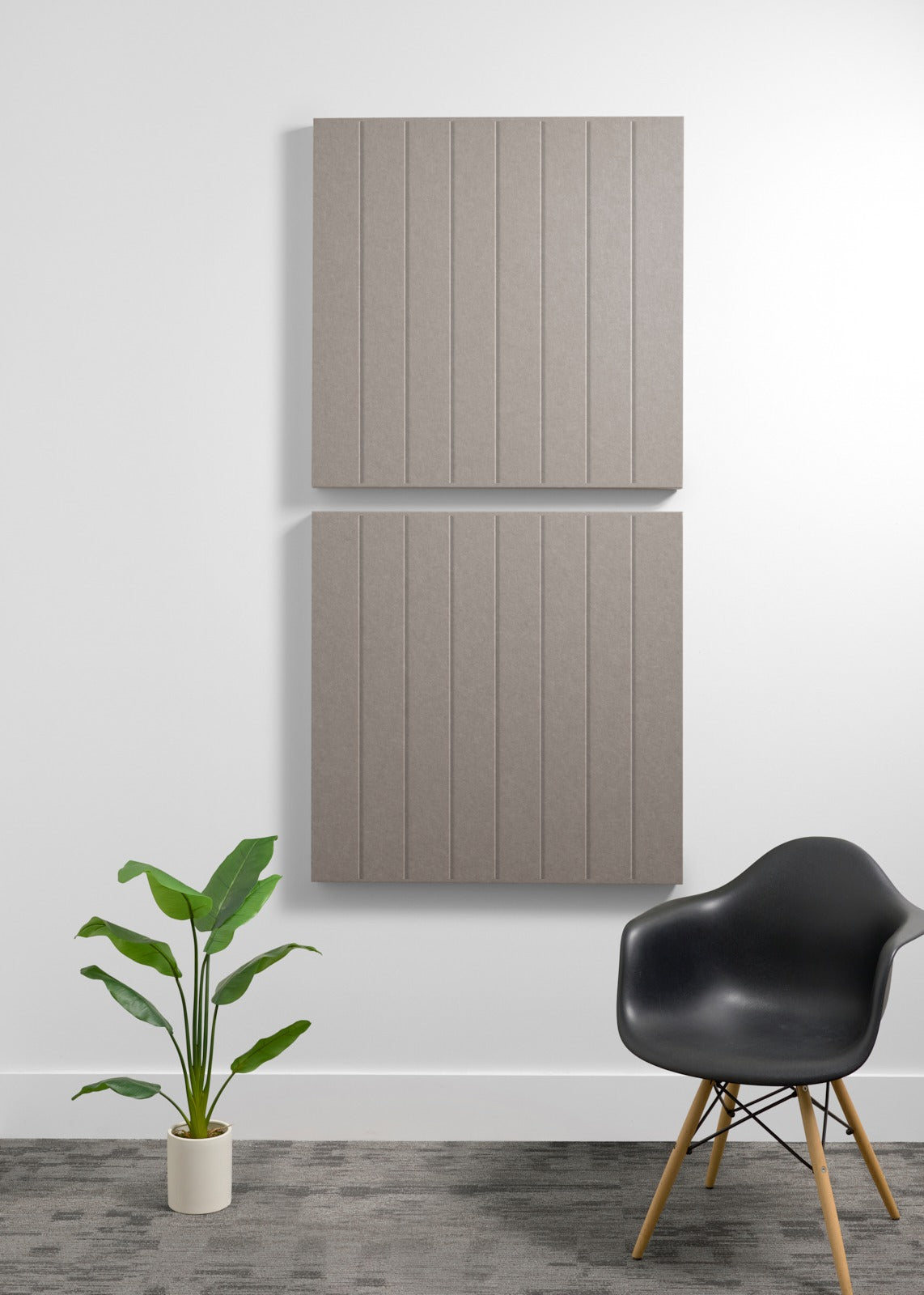 Two large beige acoustic wall panels with vertical grooves mounted on white wall above black chair and potted plant.