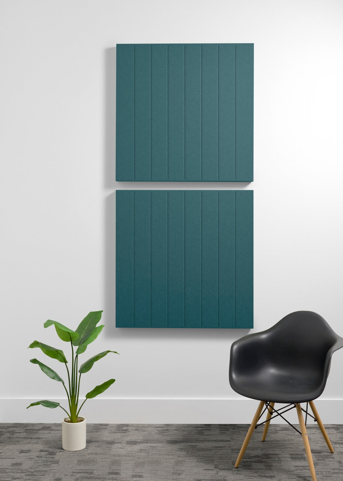 Two teal acoustic wall panels with vertical ribbed texture mounted on white wall above black chair and potted plant.