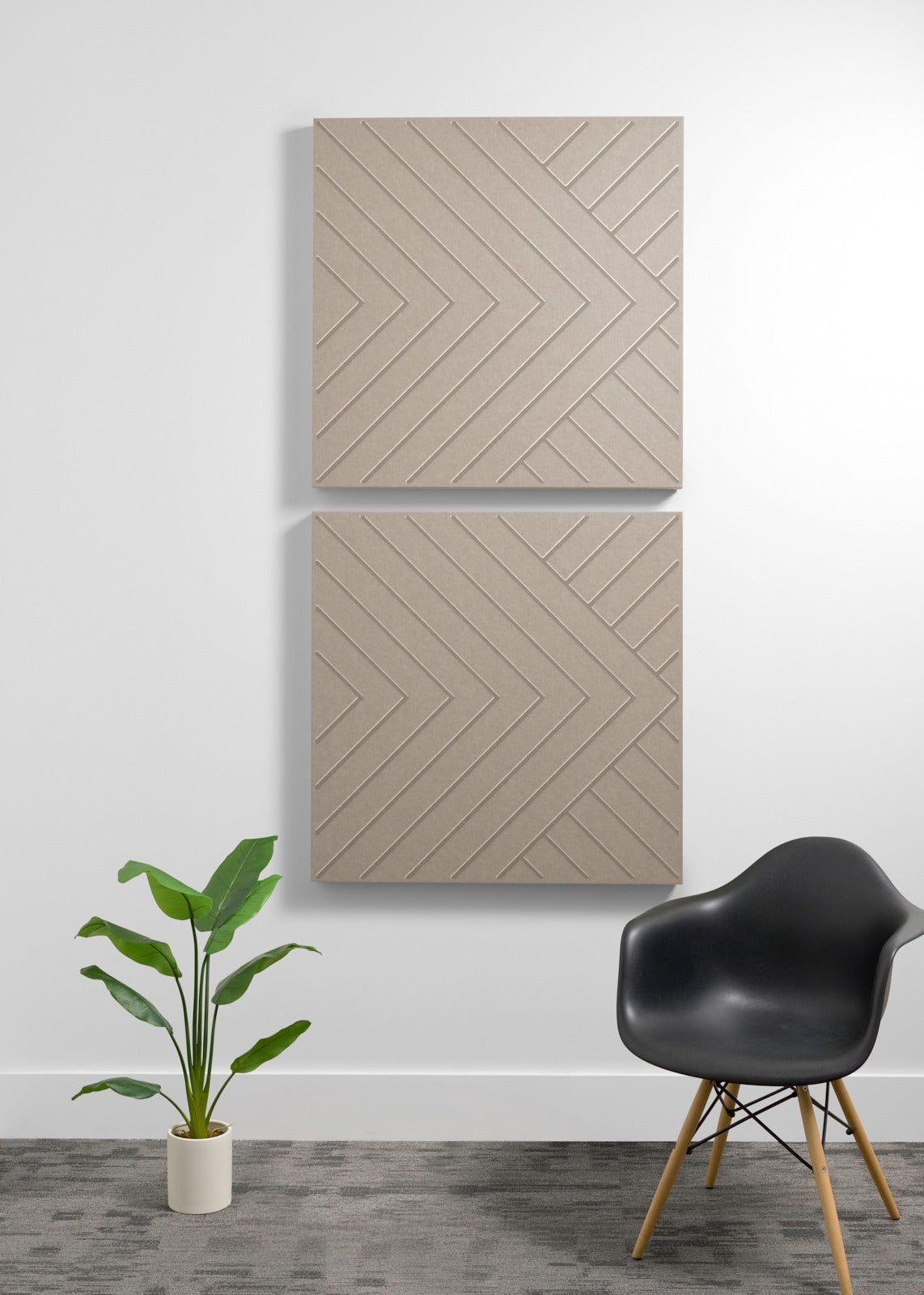 Two tan acoustic wall panels with chevron patterns mounted vertically above a black chair and potted plant.
