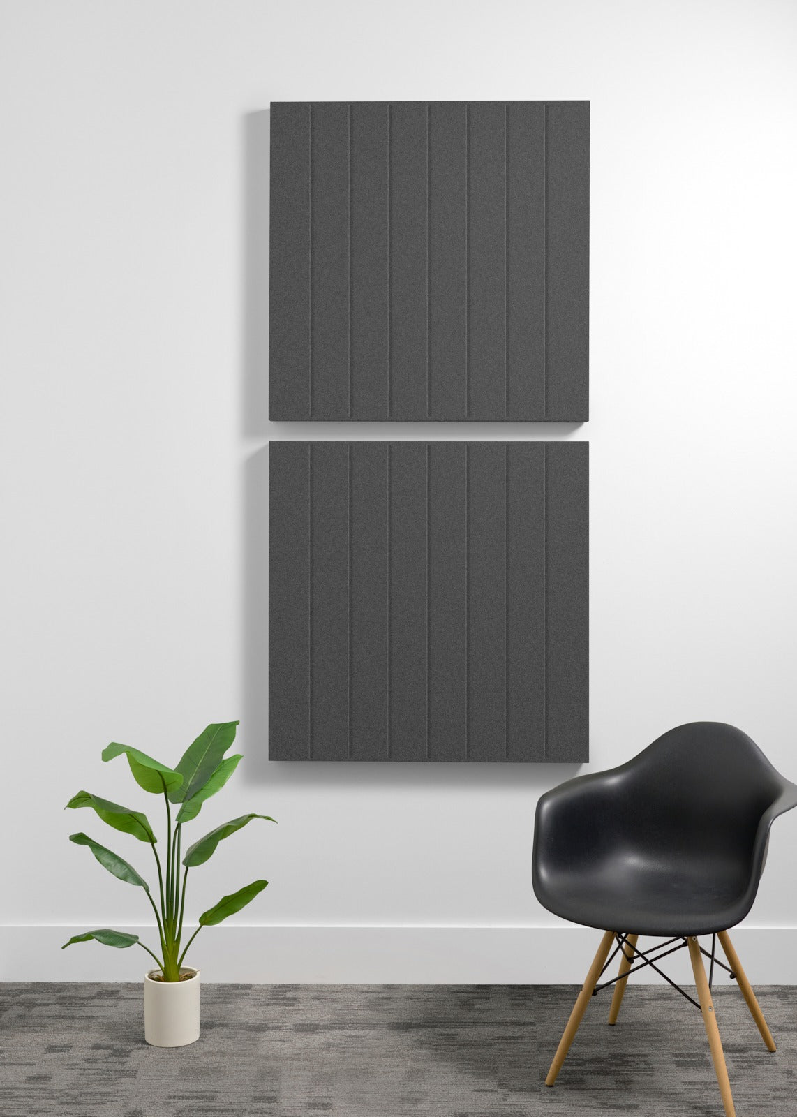 Two large dark gray acoustic panels with vertical ribbed texture mounted on white wall above modern chair and potted plant.