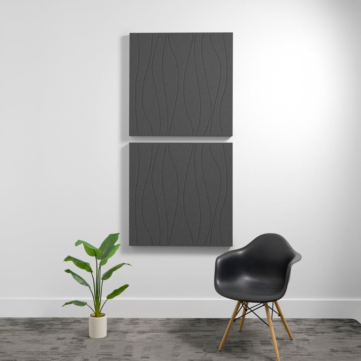 Two stacked gray acoustic panels with wavy engraved patterns mounted on white wall above chair and plant.