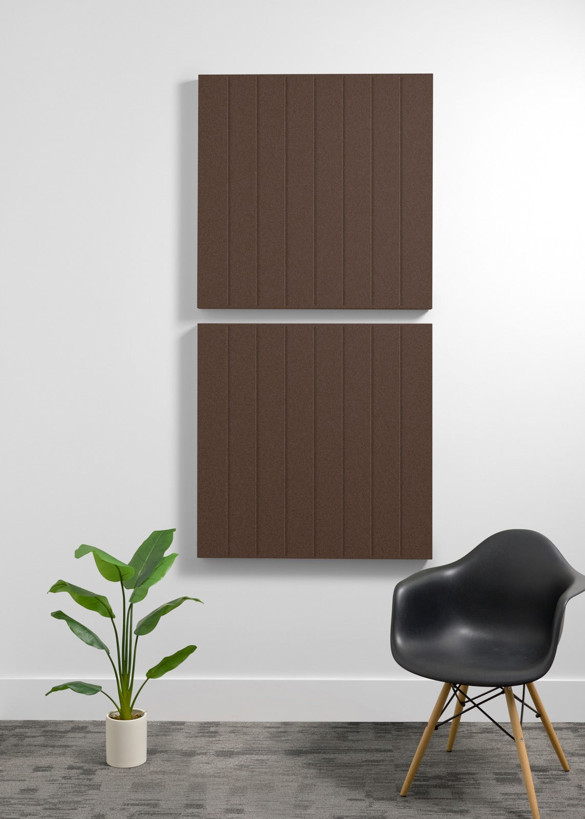 Two large brown acoustic panels with vertical ribbed texture mounted on white wall above black chair and potted plant.
